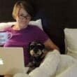 a woman sitting in bed with a laptop and a dog