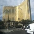 a large gold building with palm trees and people walking on the street with Mandalay Bay in the background