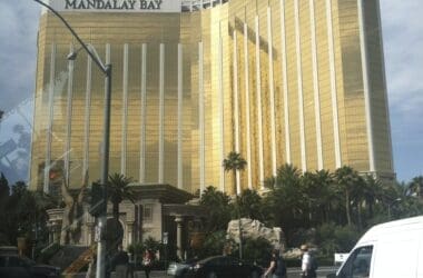 a large gold building with palm trees and people walking on the street with Mandalay Bay in the background