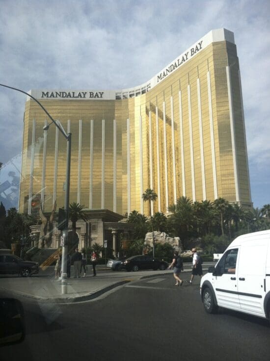 a large gold building with palm trees and people walking on the street with Mandalay Bay in the background