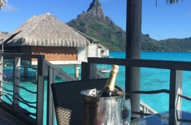 a champagne bottle and glasses on a table with a beach and water in the background