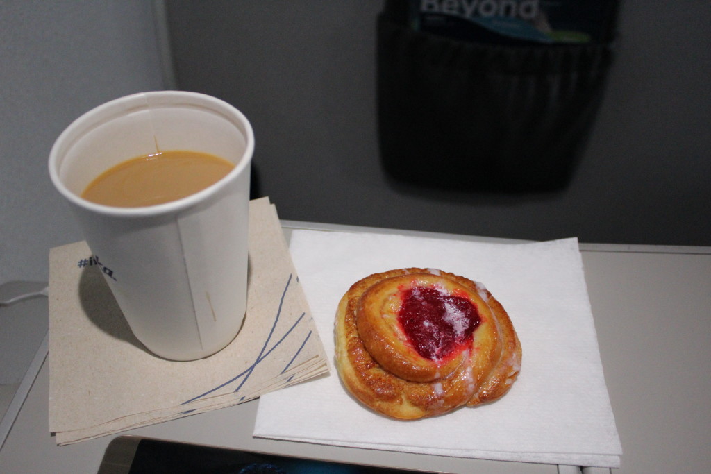 A cup of Starbucks Coffee next to a cherry pastry served in Alaska Airlines First Class on a flight from Dallas to Portland, Oregon.