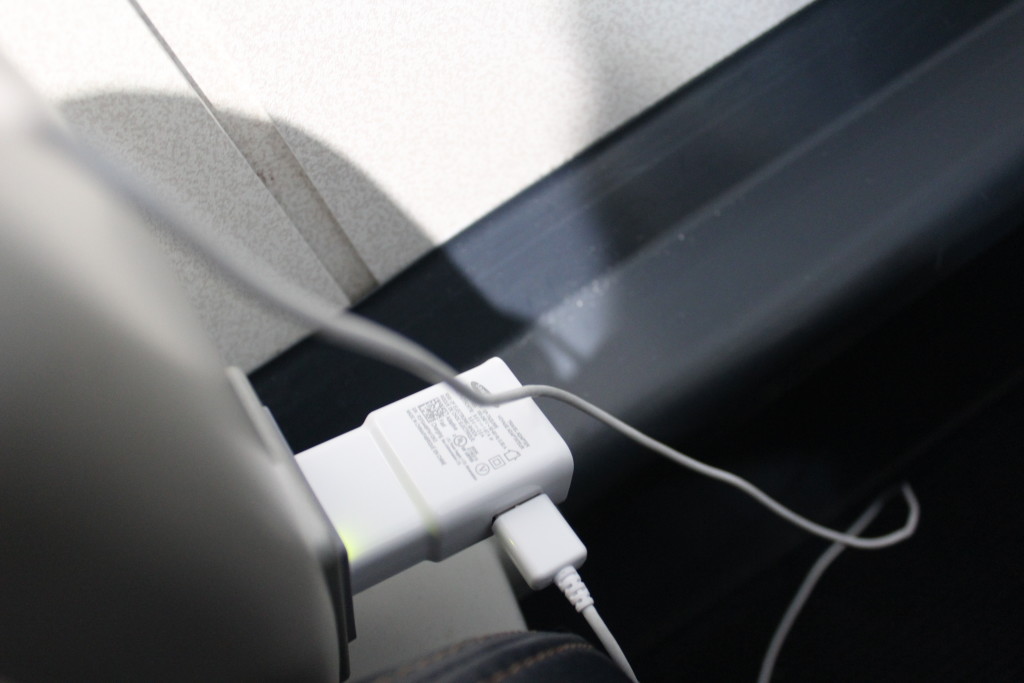 A phone charger plugged into a power outlet aboard an Embraer E175 passenger aircraft