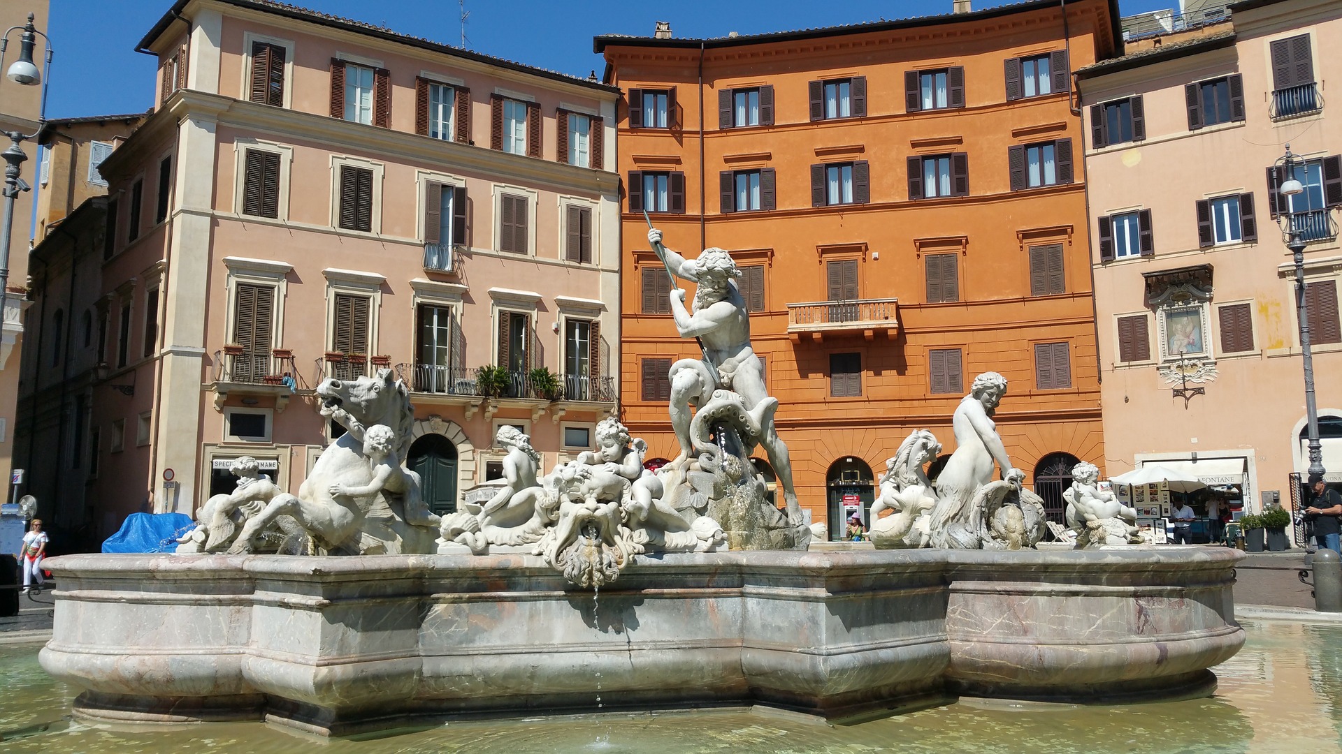 a fountain with statues in front of buildings with Piazza Navona in the background