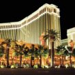 a large building with palm trees at night with The Venetian Las Vegas in the background