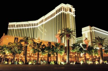 a large building with palm trees at night with The Venetian Las Vegas in the background