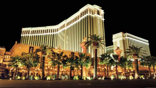 a large building with palm trees at night with The Venetian Las Vegas in the background