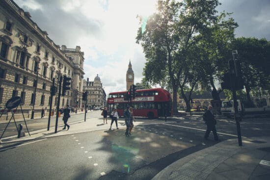 a red double decker bus on a street with people walking around