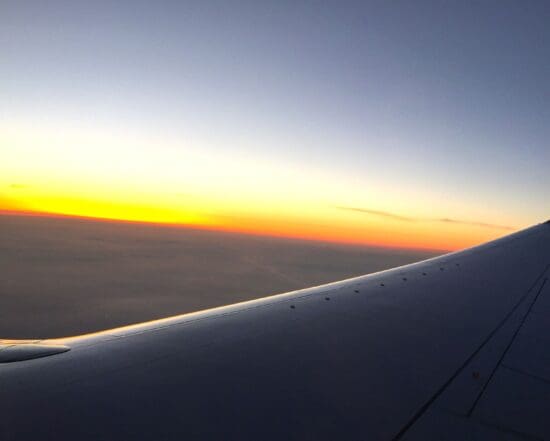 an airplane wing with the sun setting in the background