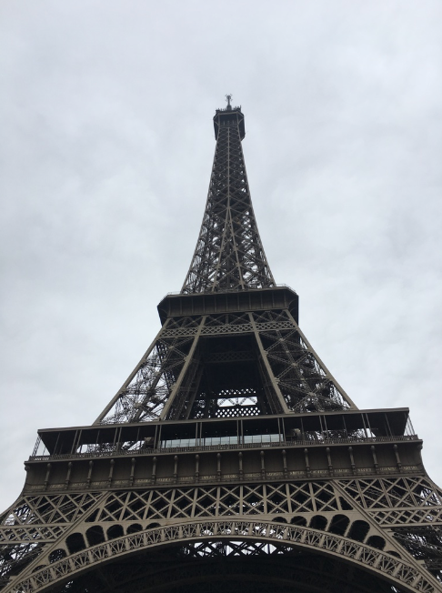 a tall metal tower with a cloudy sky with Eiffel Tower in the background