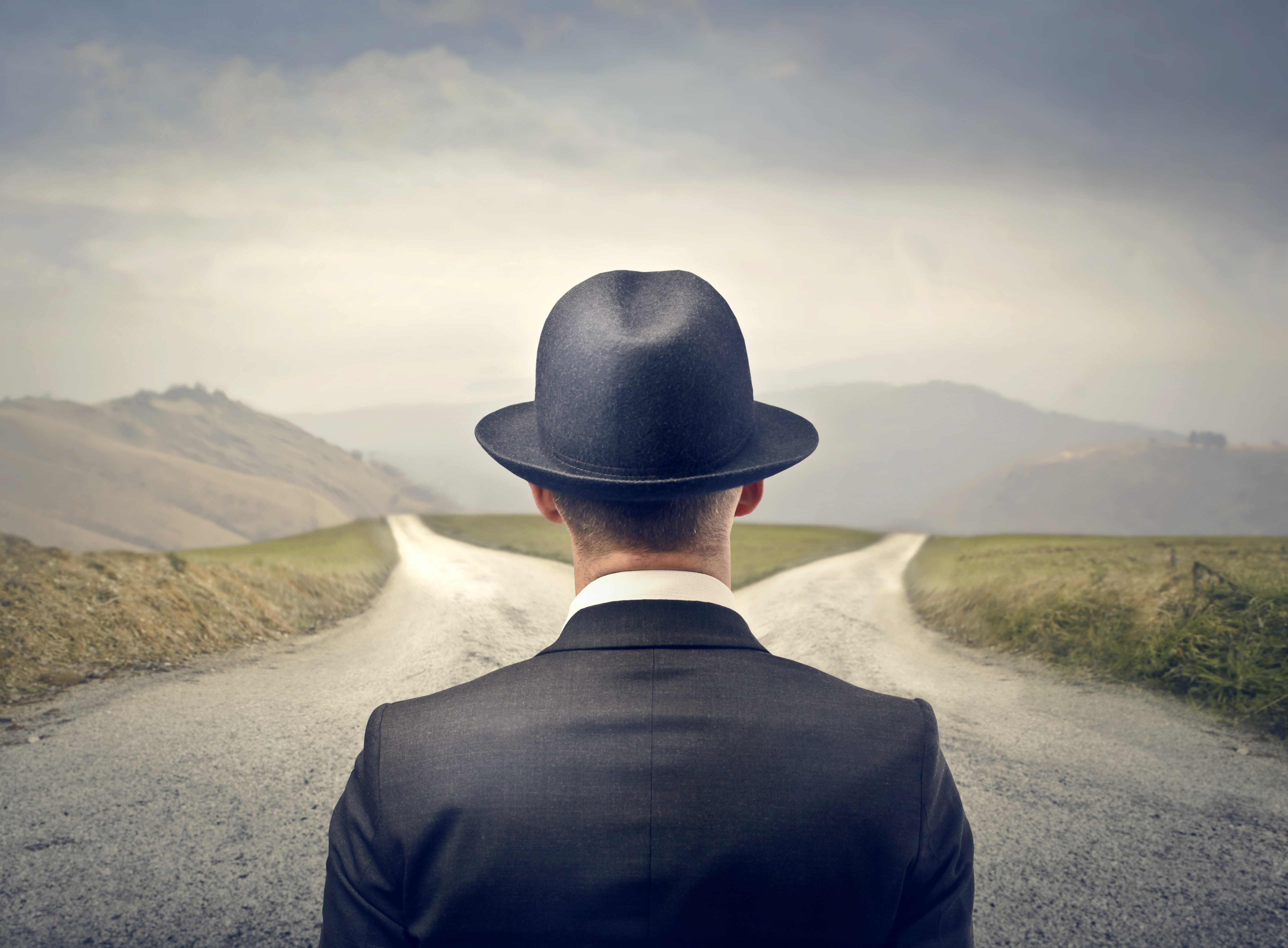 a man in a suit and hat looking at a road