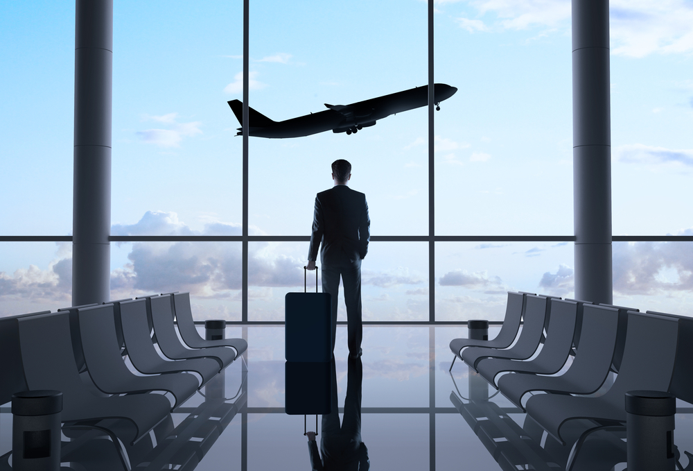 a man standing in an airport with a suitcase looking out the window