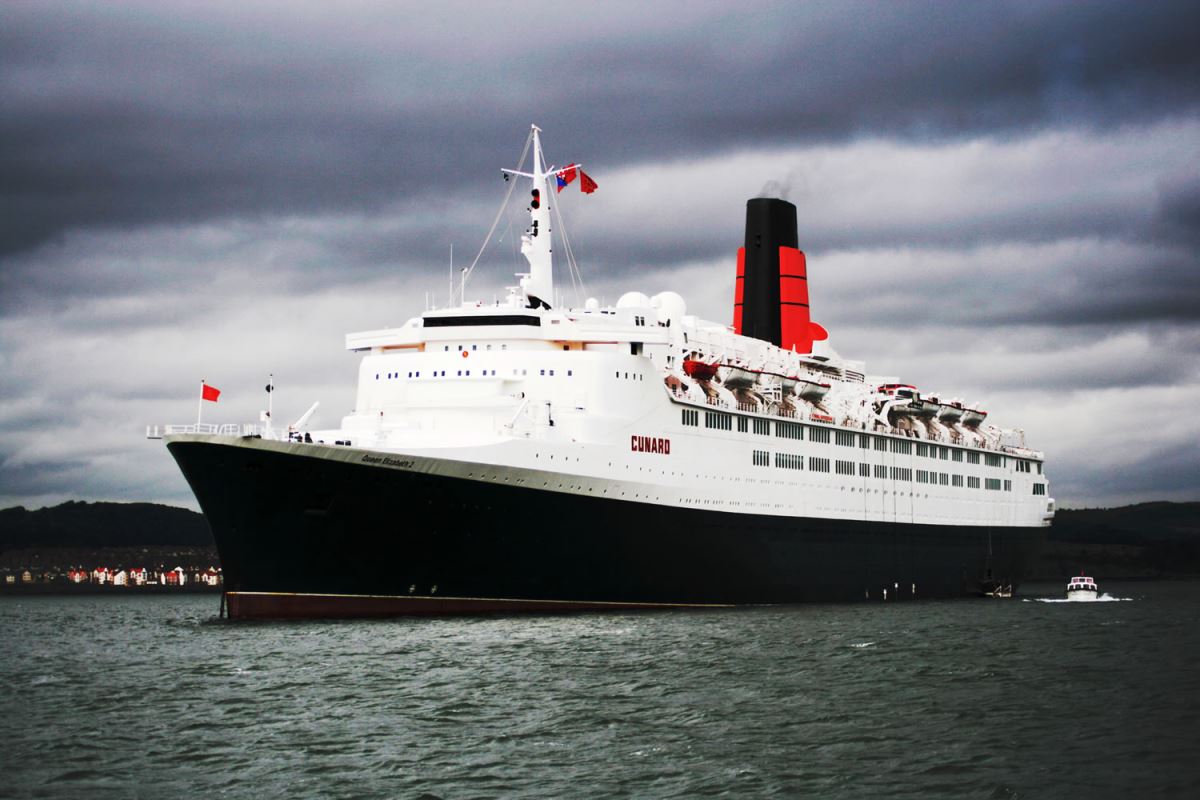 a large ship in the water with RMS Queen Mary in the background