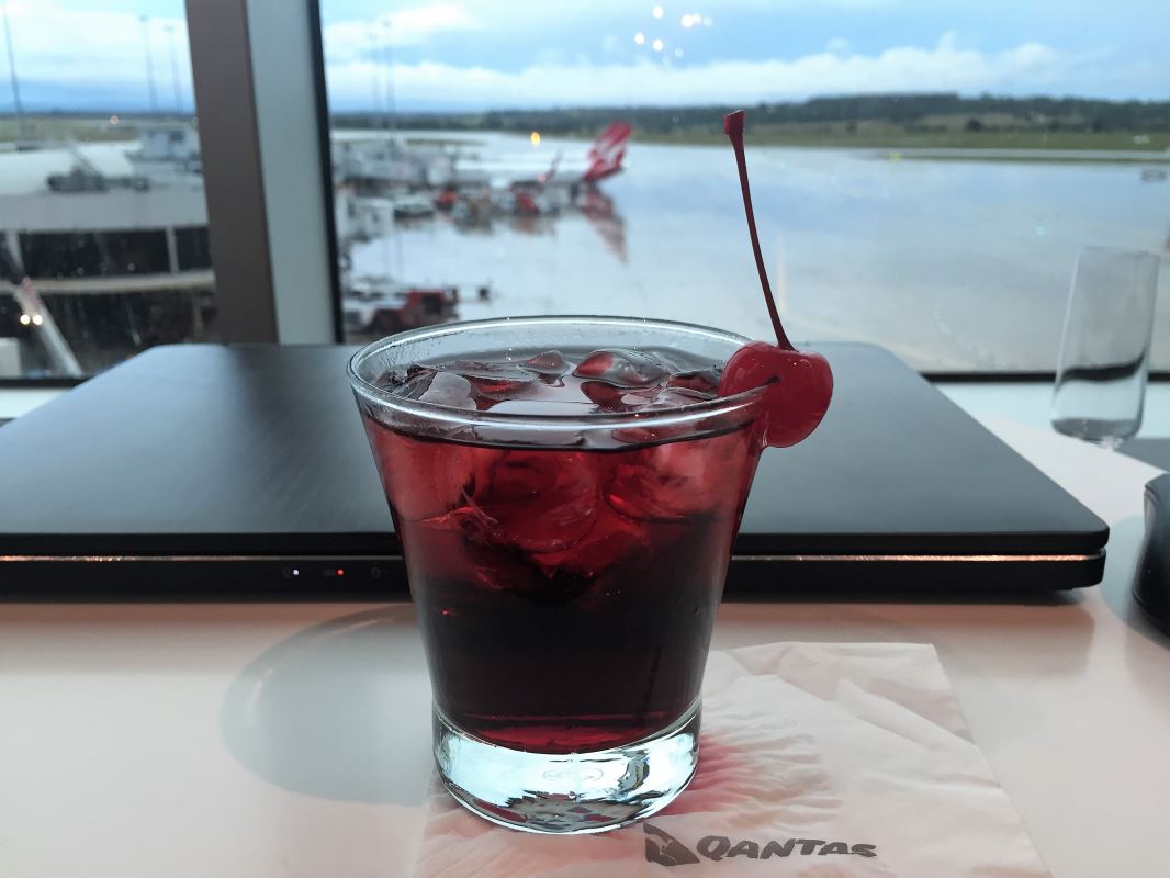 a glass of red liquid with ice and a cherry on top