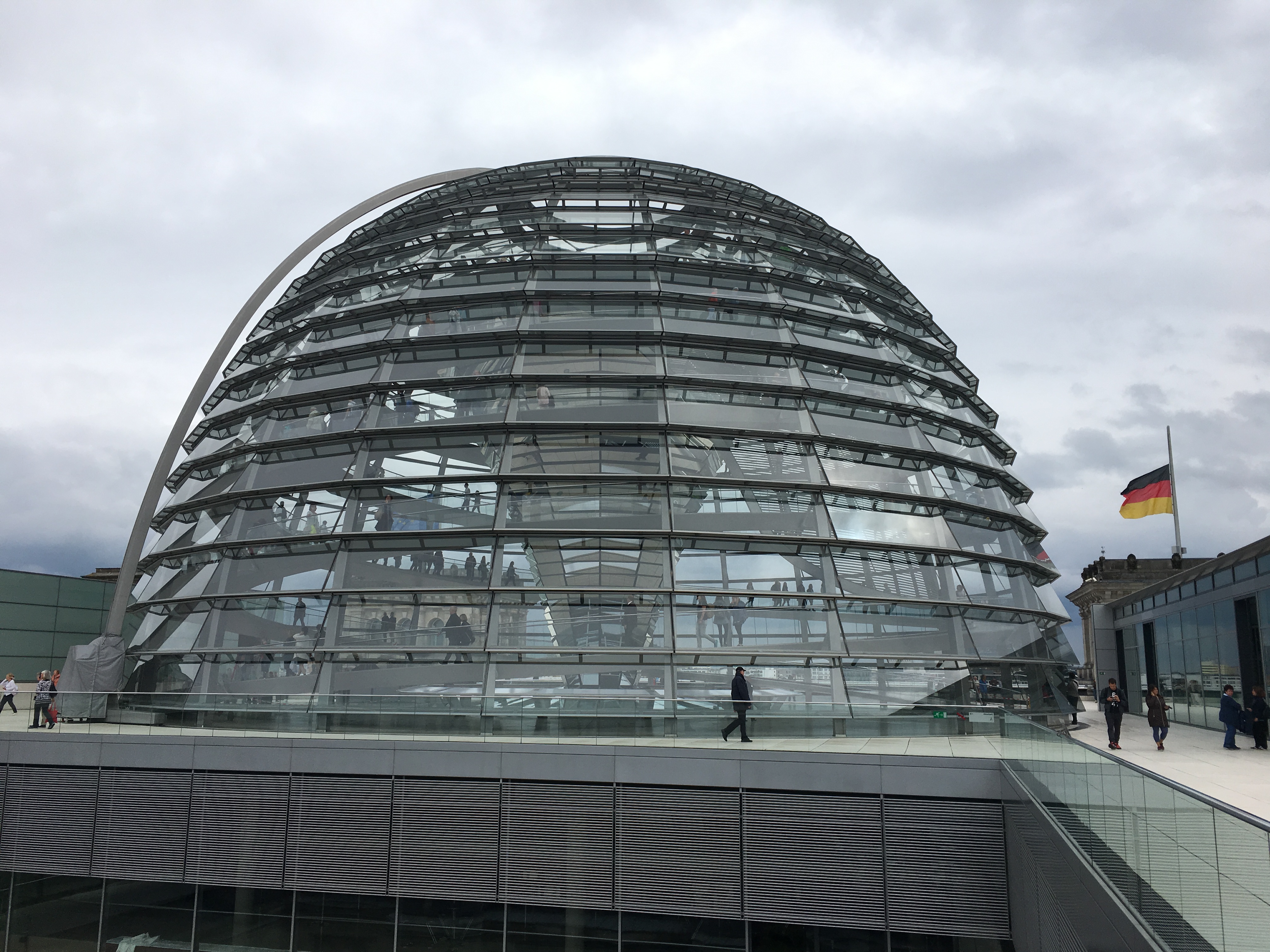 a glass dome with people walking on the ground with Reichstag dome in the background