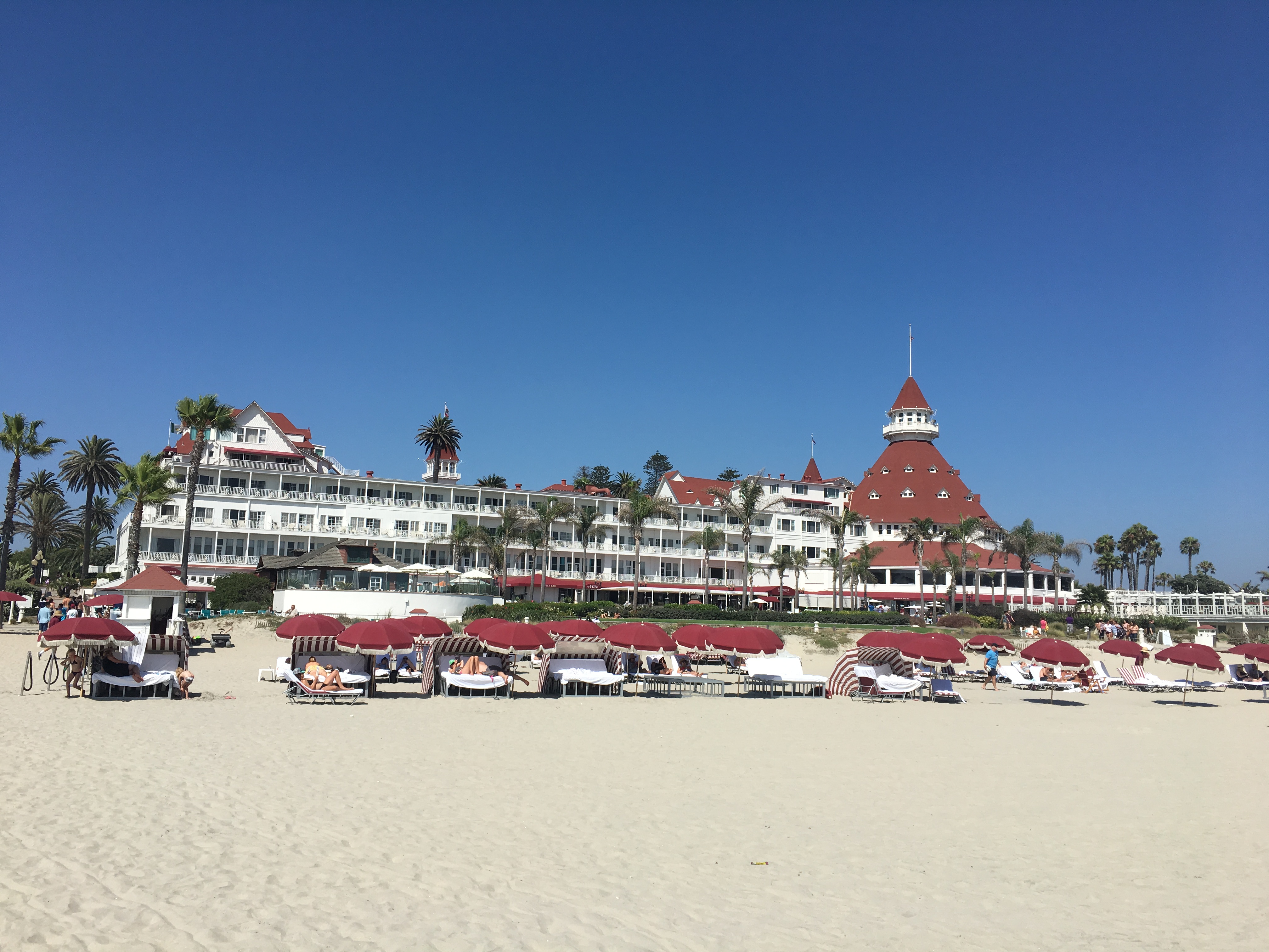 a large building with red roofs on a beach with Hotel del Coronado in the background