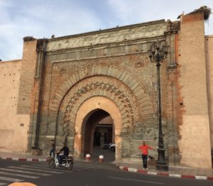 a brick archway with people walking on the street with Bab Agnaou in the background