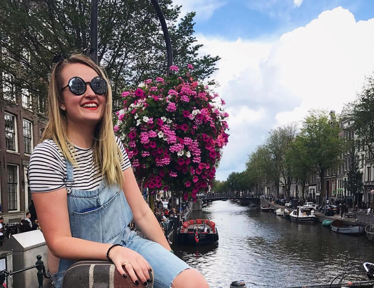 a woman sitting on a railing with a river and flowers