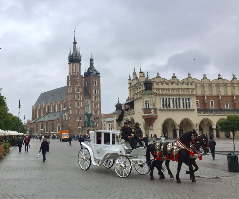 a horse carriage with people on it with Main Square, Kraków in the background