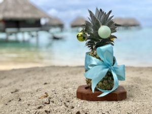 a pineapple with a blue bow on sand
