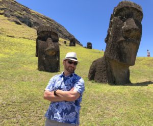 a man standing in front of a group of statues with Easter Island in the background