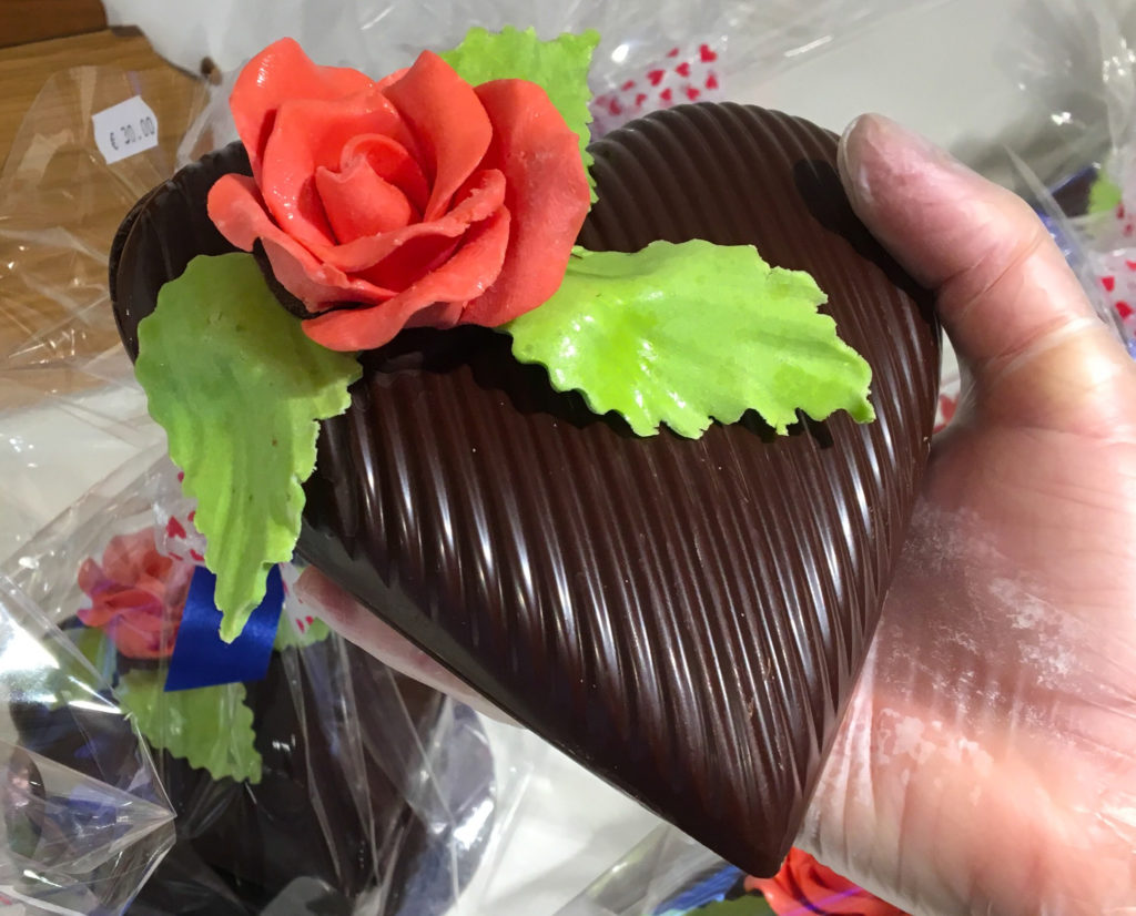 a hand holding a chocolate heart with a rose