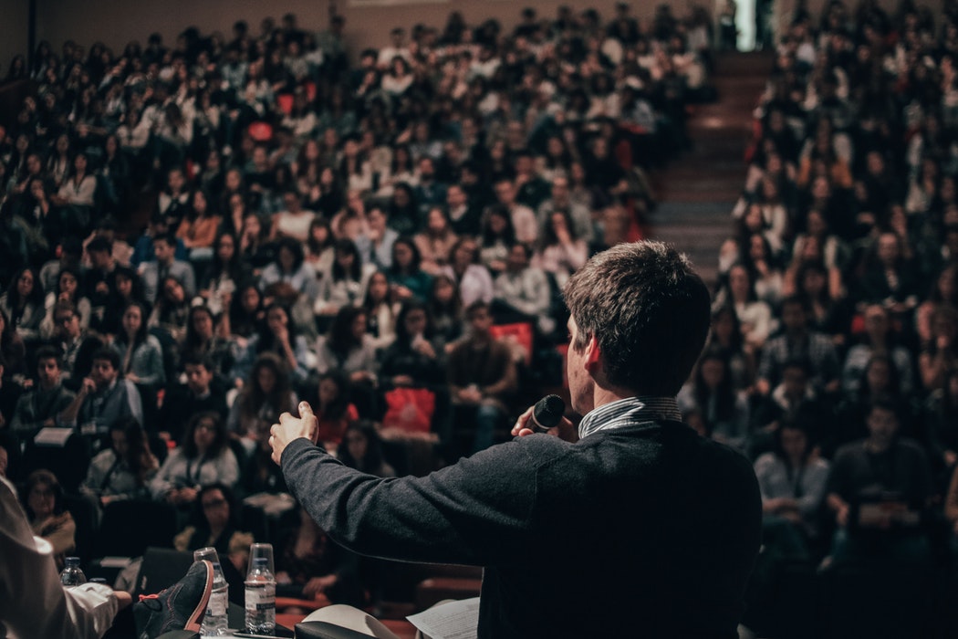 a man speaking into a microphone in front of a large crowd