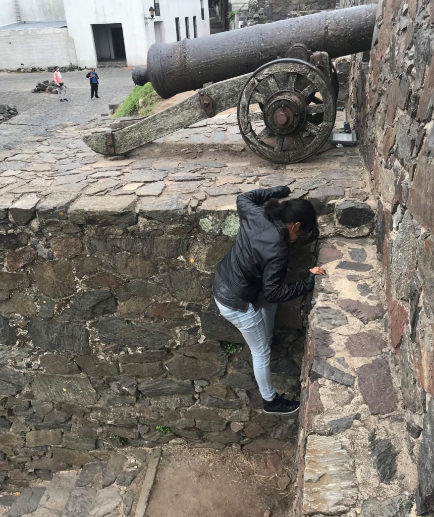 a woman leaning on a stone wall with a cannon