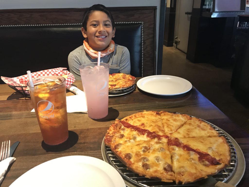 a boy sitting at a table with pizzas