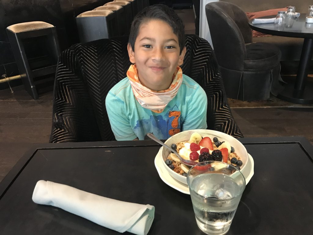 a boy sitting at a table with a bowl of fruit and a glass of water