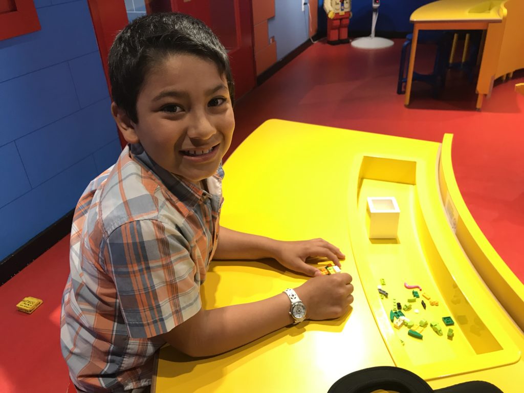 a boy sitting at a table with lego pieces