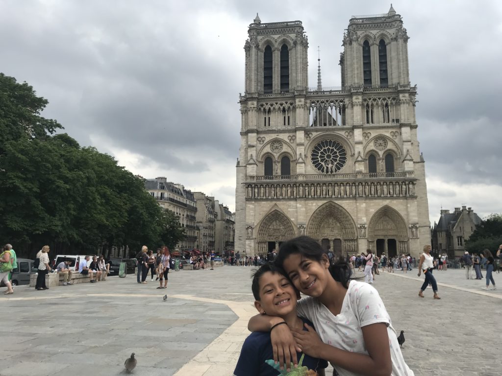 a boy and girl posing for a picture in front of a large building with Notre Dame de Paris in the background