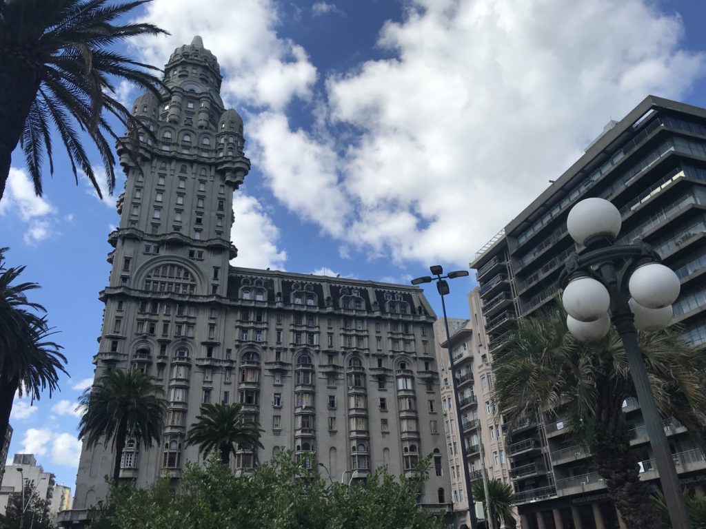 a tall building with a tall tower and palm trees with Palacio Salvo in the background