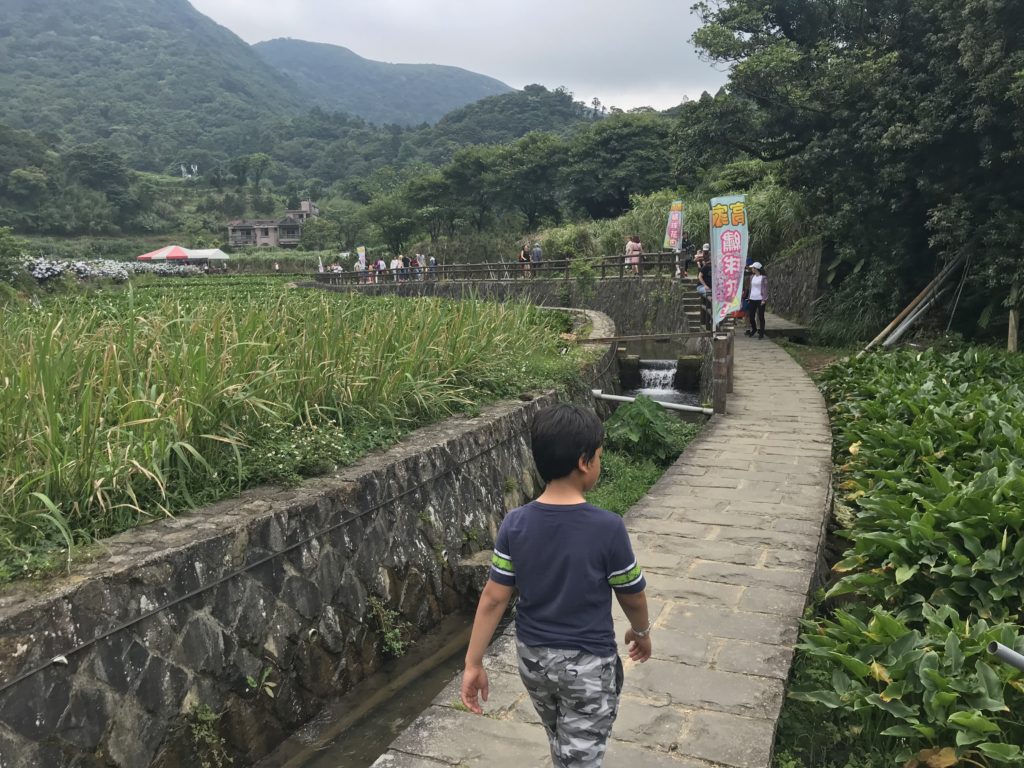 a boy walking on a path with a stream and people in the background