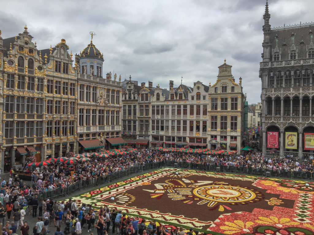 a large crowd of people in a square with a carpet of flowers with Grand Place in the background