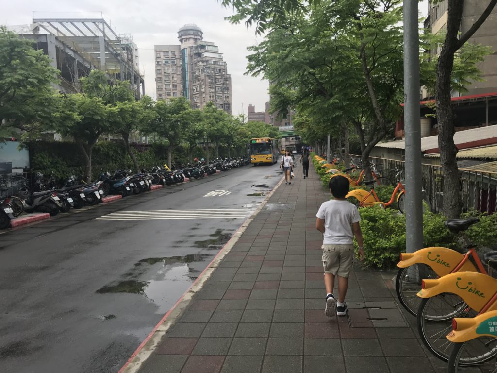 a boy walking on a sidewalk with bikes and trees