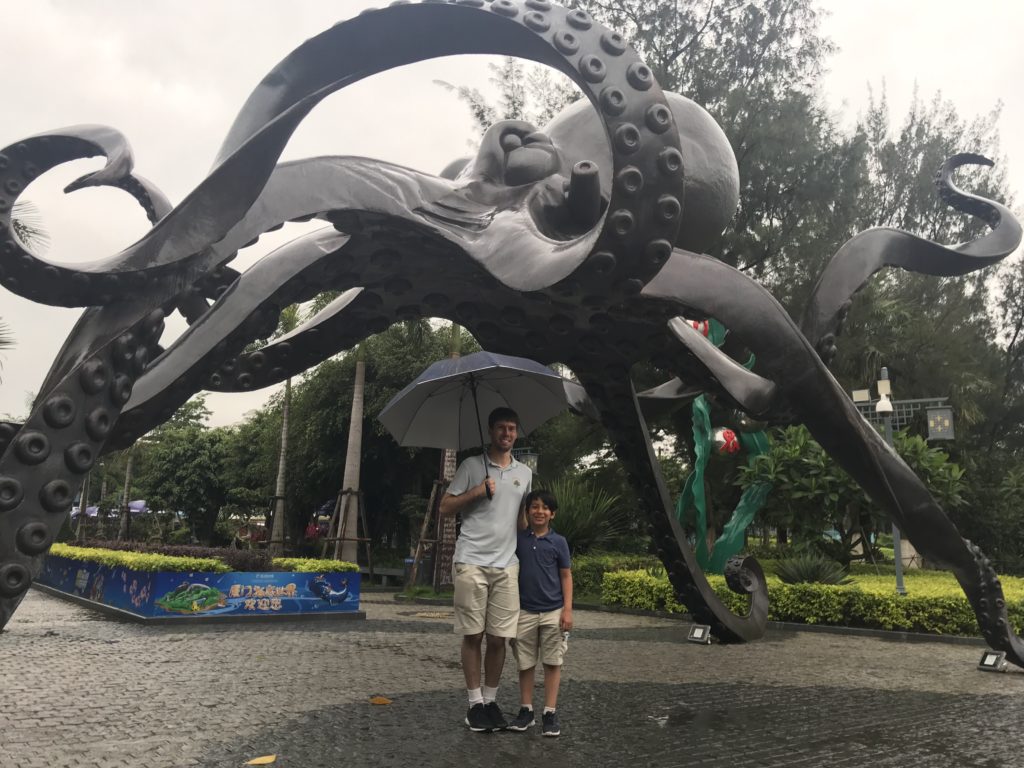 a man and boy standing under an umbrella under a large octopus statue
