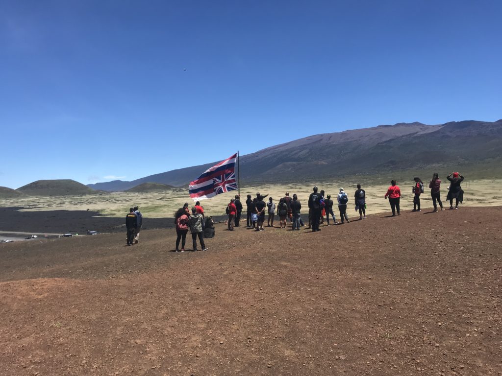 a group of people standing on a dirt hill with a flag