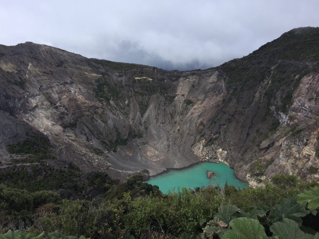 a blue lake surrounded by mountains with Irazú Volcano in the background
