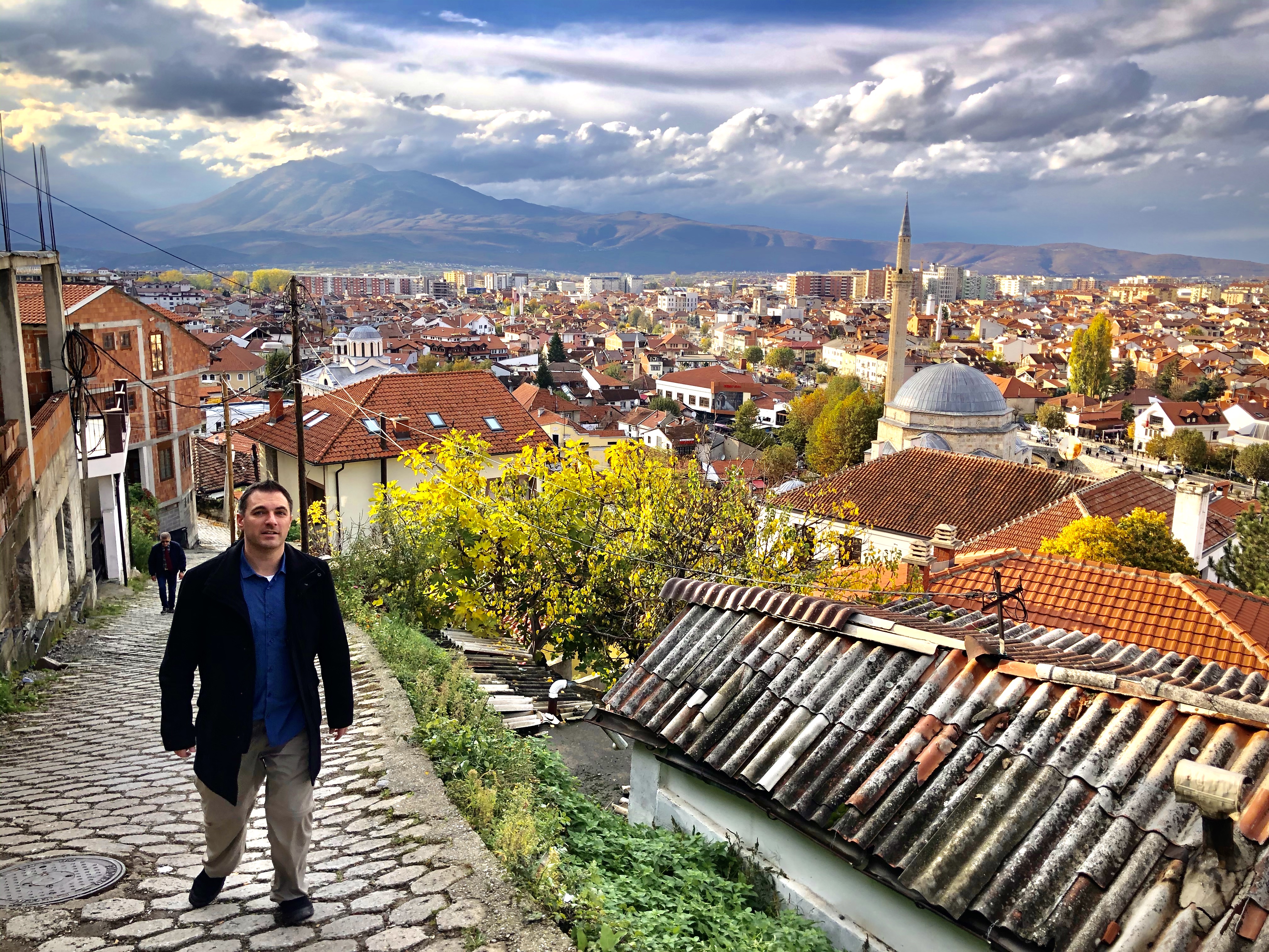 a man standing on a stone path with a city in the background