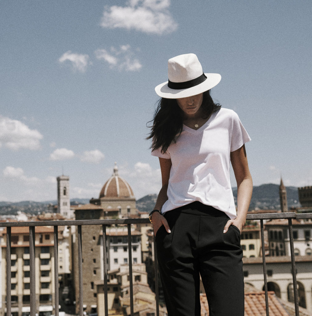 a woman standing on a balcony with a white hat and a city in the background