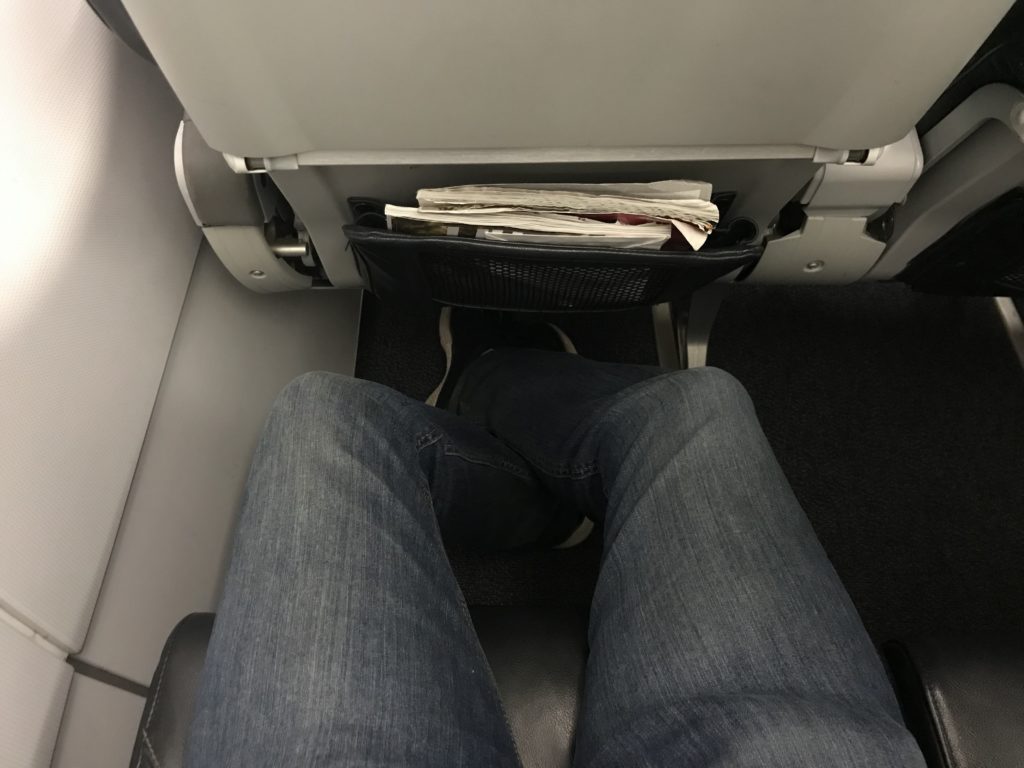 a person's legs in jeans and a pocket with papers in the back of a seat