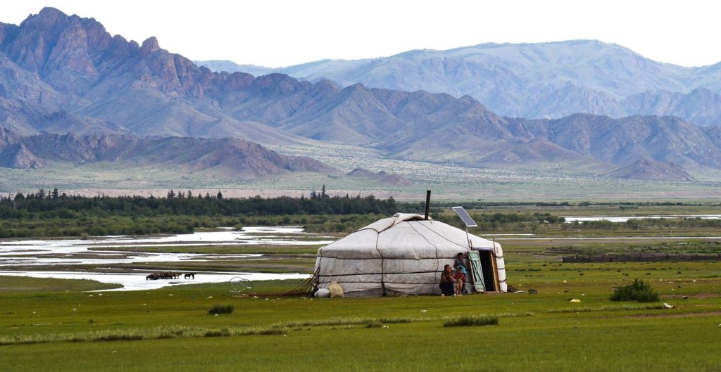 a yurt in a field with mountains in the background