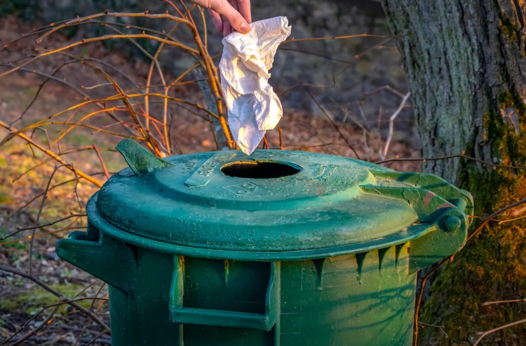 a hand throwing a tissue into a green trash can