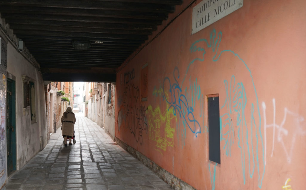 a person walking down a walkway with graffiti on the wall