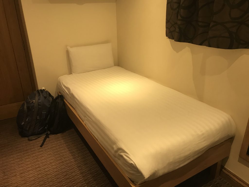 a bed with a white sheet and a backpack