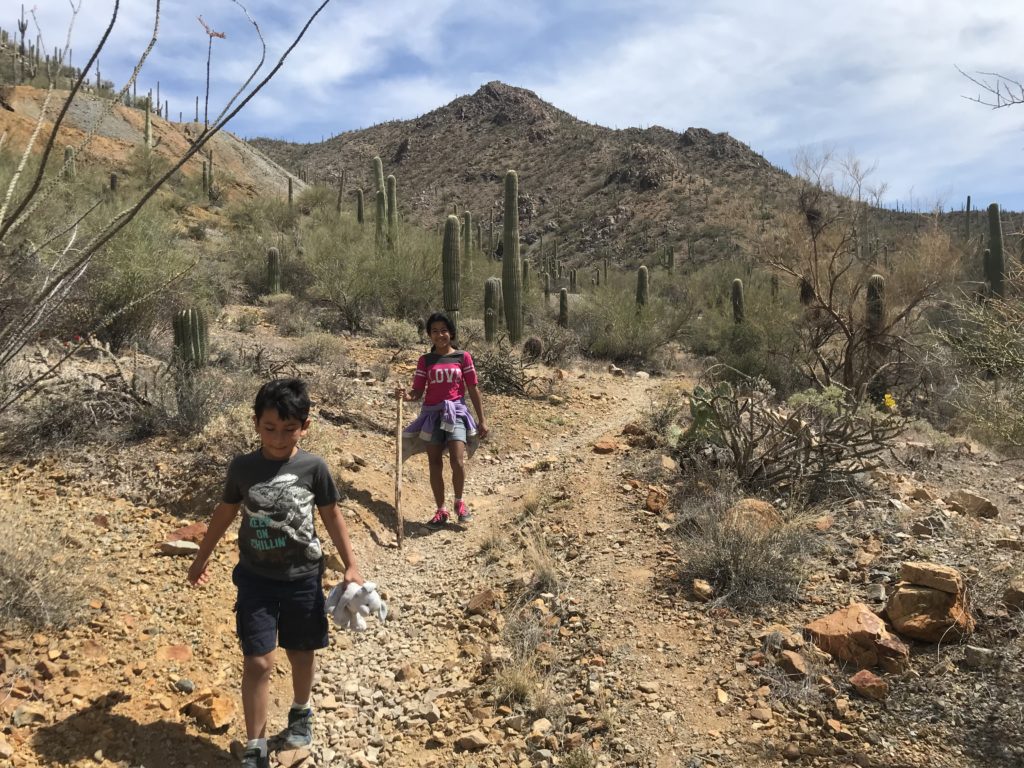 a boy and girl walking on a dirt path with cactuses