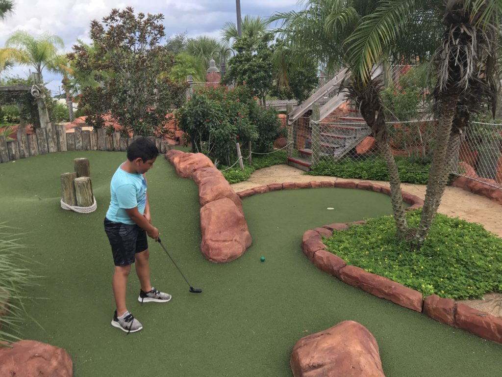 a boy playing golf in a miniature golf course