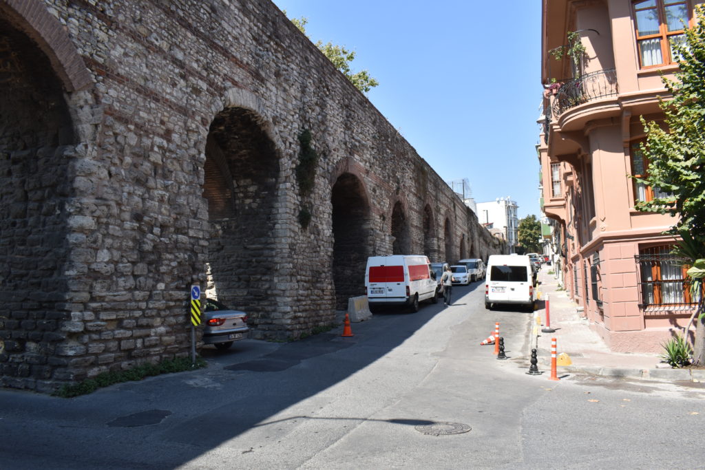 a stone wall with arches and cars parked on the side