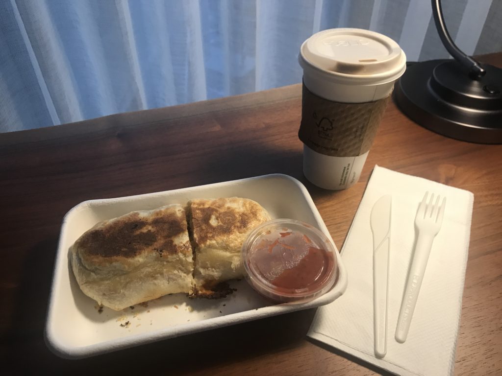 a food in a styrofoam container with a cup of coffee and a napkin